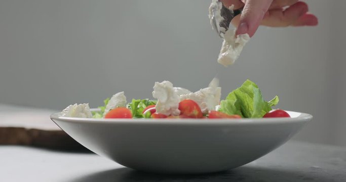 Slow motion add ricotta cheese to cherry tomatoes and frisee leaves into white bowl