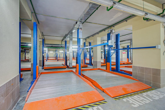 Hydraulic Lift Or Mechanical Jack For Repair And Storage Of Car In Underground Parking. Modern Underground Parking Without Cars. Signs And Boards Indicating Directions. 