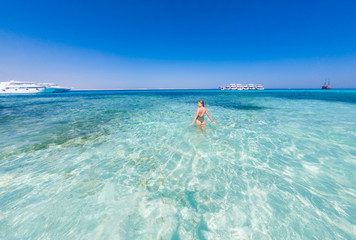 Fototapeta na wymiar A girl in a green swimsuit to bathe in the blue water of the red sea. It's sunny outside
