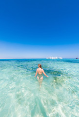 Fototapeta na wymiar A girl in a green swimsuit to bathe in the blue water of the red sea. It's sunny outside