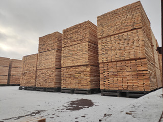 Natural wood boards stacked in a stack at an open lumber warehouse in the snow