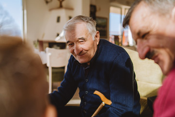 Portrait of senior man 80 years old pensioner sitting in chair with his family son and grandson at...