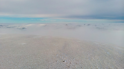 A aerial scenic view of a snowy mountain summit and mountain range in the background under a majestic blue sky and some altitude white cloud