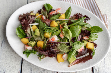 Mango salad with green mix, shrimps and avocado on a white plate.