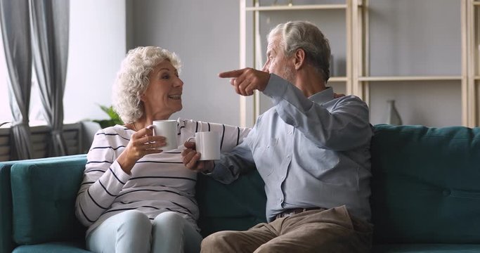 Smiling elderly woman drinking hot coffee with husband at home.