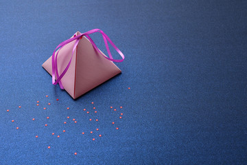 Festive background for Valentine's Day, International women's day, Christmas and New year. Holiday card, with a pink pyramidal gift box on a blue silver background with red stars, space for text.