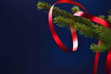 Spruce branch with a red ribbon on a dark blue background and space for text.