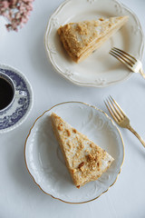 two pieces of cake on white plates golden forks a vase with a flower and a golden candlestick on a white table