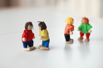 Group of four wooden flexible children puppets in colourful clothes standing on a white table 