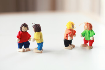 Group of four wooden flexible children puppets in colourful clothes standing on a white table 