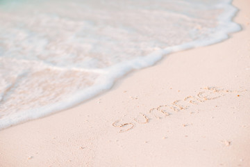 Fototapeta na wymiar Word Summer handwritten on sandy beach with soft ocean wave on background