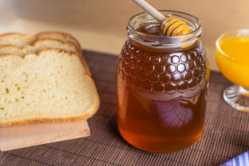 Still life with natural honey, orange juice, rustic bread and honey spoon falling on the honey jar
