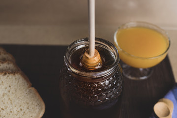Still life with natural honey, orange juice, rustic bread and honey spoon falling on the honey jar