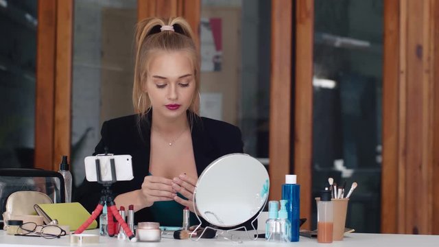 Gorgeous beauty blogger confidently applying lipstick while recording make-up tutorial video for internet