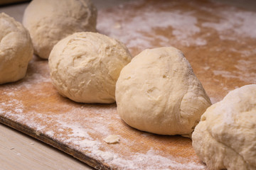 Balls of dough. Plywood cutting board, wooden flour sieve and wooden rolling pin - tools for making dough.