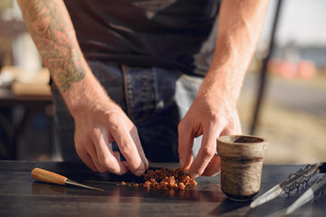 A person takes tobacco. The person is preparing a hookah. There is a table.