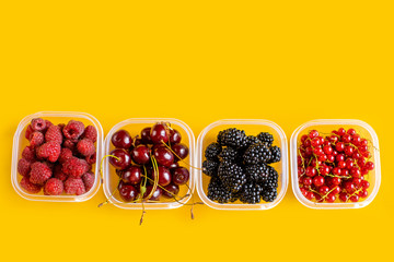 4 plastic plates, containers with raspberry, blackberry, red currant, cherry on a yellow background.