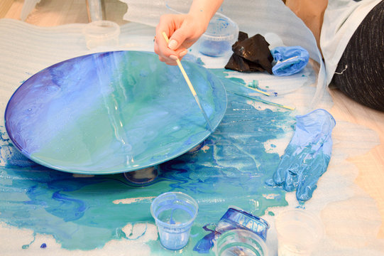 The Process Of Creating A Home-made Trendy Abstract Modern Pattern Painted With A Brush Of Acrylic Blue Multi-colored Resin On A Round Wooden Board