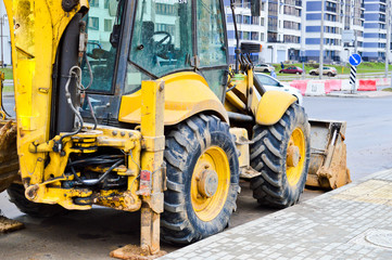 Big bright yellow powerful industrial heavy excavator tractor, bulldozer, specialized construction equipment for road repair during the construction of a new micro-district in a big city
