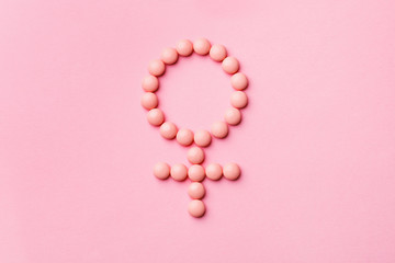 pink medicine tablets shaped as gender symbol on pastel rose background, venus sign, top view, flat...