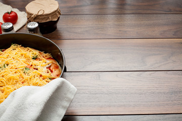 The pizza is completely strewn with cheese, before being sent to the oven in hands in a potholder, on a wooden background, with copy space. The concept of cooking pizza, homemade recipes for food.