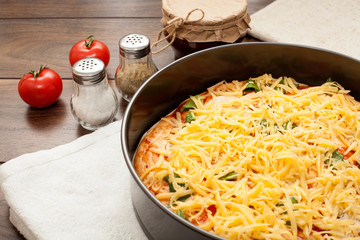 The pizza is completely strewn with cheese, before being sent to the oven in hands in a potholder, on a wooden background. The concept of cooking pizza, homemade recipes for food.