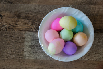 Easter eggs in a white bowl on brown wooden floor