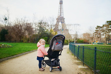 baby girl standing next to her pushchair in Paris near the Eiffel tower