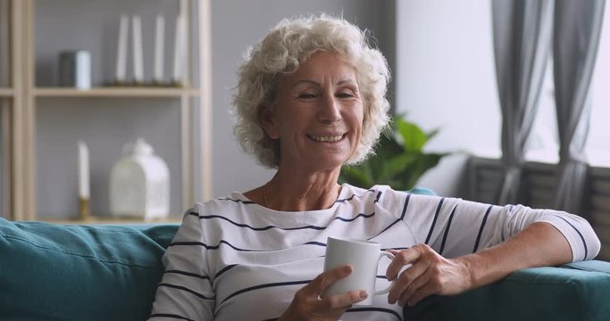 Happy older grandmother resting on cozy sofa.