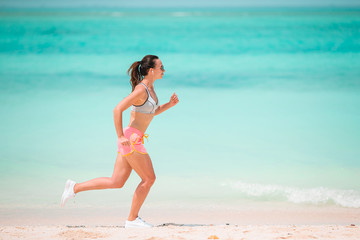 Fit young woman doing exercises on tropical white beach in her sportswear