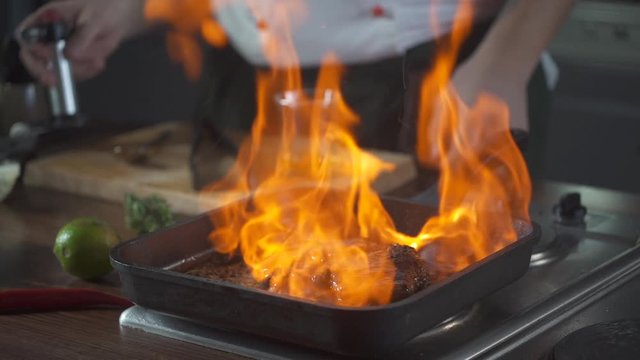 Chef making steak fillet mignon in flambe style on a grill pan. Oil and alcohol fire with open flames. Food on cuisine. Nutrition in gourmet kitchen. Making meal. Prepare food to eat. Delicious dish.