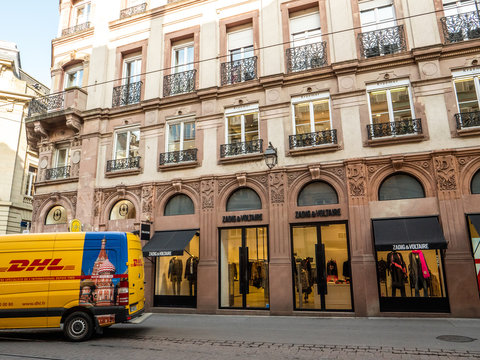 STRASBOURG, FRANCE - OCT 26, 2018: DHL Deutsche Post yellow delivery van parked on the street in france in front of the luxury fashion clothes store Zadig and Voltaire