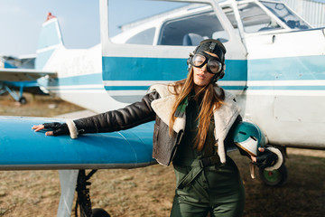 a girl with glasses and a headdress holds a helmet in her hands, in the background of the plane she...