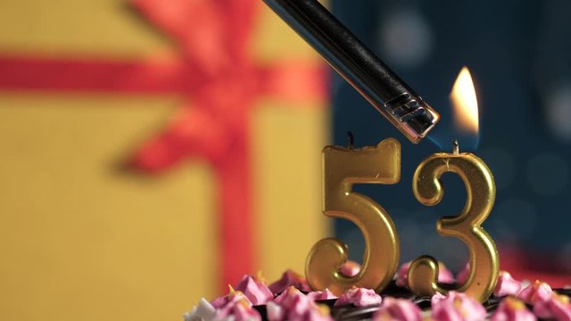 Birthday cake number 53 golden candles burning by lighter, blue background gift yellow box tied up with red ribbon. Close-up and slow motion