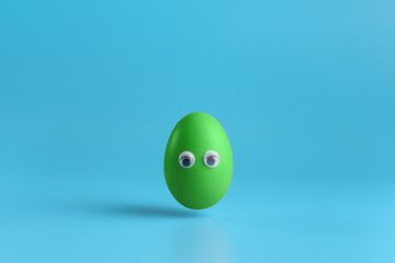 One green egg  with eyes on a blue background. Minimal Happy Easter concept decoration. Copy space for text mockup.