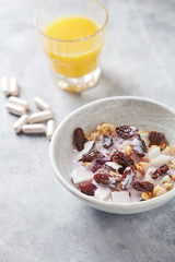 Bowl of granola with yogurt, nuts,  cranberry, almonds and rasins. Sport supplements ( carnitine capsules ) in background. Bright stone  background. 