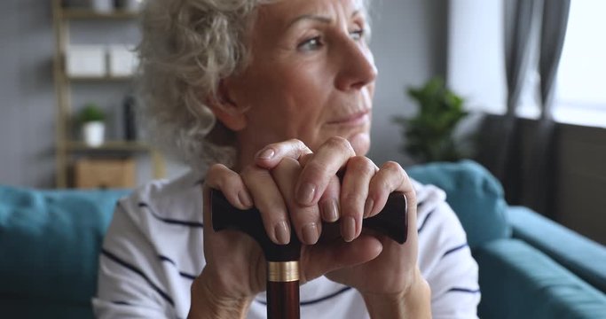 Focus on older hoary woman holding hands on walking stick.