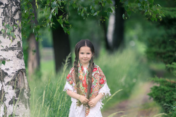 Portrait of a little beautiful girl in a birch grove. Her shoulders are covered with a shawl with...