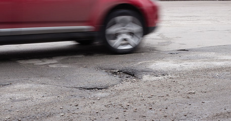 The car goes around a pothole on the road. Broken asphalt after winter.