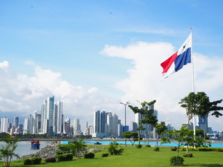 Panama City / Panama - September 1 2019: City skyline with green grass and flag flying. Blue sky and white clouds. - obrazy, fototapety, plakaty