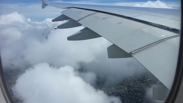 Impressive aerial view from airplane window on air plane wing flying high over white fluffy clouds in clear blue sky