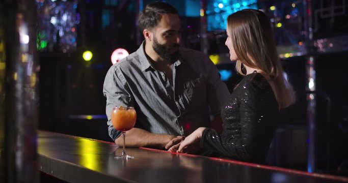 Confident young Middle Eastern man coming to charming Caucasian girl dancing next to bar counter. Handsome guy flirting with beautiful woman in night club. Cinema 4k ProRes HQ.