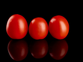 Three red tomatoes on a black glossy background