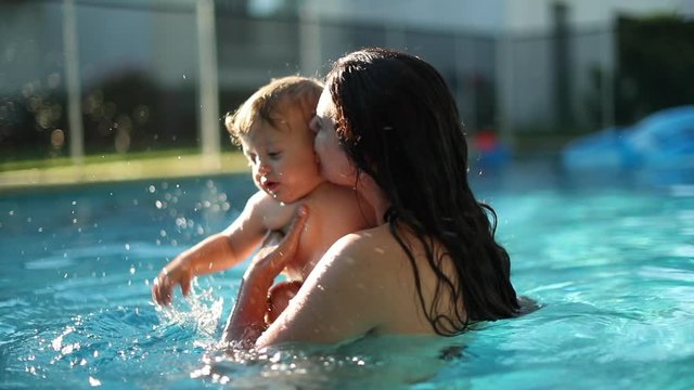 Mother kissing and caring baby infant toddler at the swimming pool water