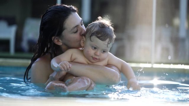 Mother kissing baby toddler at the swimming pool. Mom embracing holding and caring for infant, casual and candid