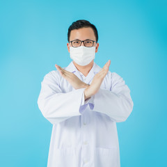 Portrait of Asian medical male Doctor wear a mask to prevent germs and standing and raising hand to show the symbol of wrong isolated on blue background.Concept of preventing infectious diseases.