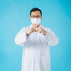 Portrait of Asian medical male Doctor wear a mask to prevent germs and standing and raising hand to show the symbol of wrong isolated on blue background.Concept of preventing infectious diseases.