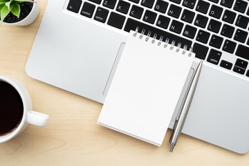 Blank notebook is on top of laptop computer over wood office desk table with pen and cup of coffee....