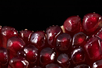 Macro photo: juicy red pomegranate seeds are pressed tightly against each other and shine. Photo in a studio on a black background with two light sources. Background for text and decoration.