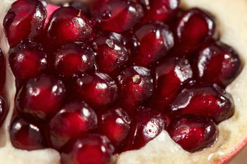 Close-up: A slice of peeled pomegranate lies on a light wood kitchen board. Bright red grains of pomegranate shine beautifully. Studio photography under artificial lighting with two light sources.